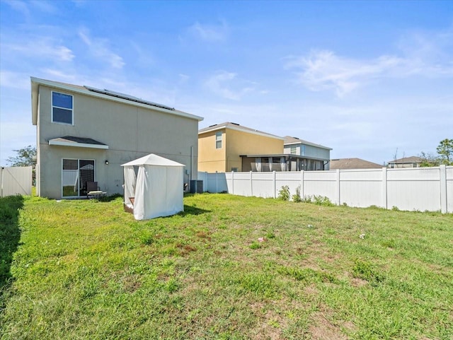 back of house with cooling unit, a lawn, fence, and roof mounted solar panels