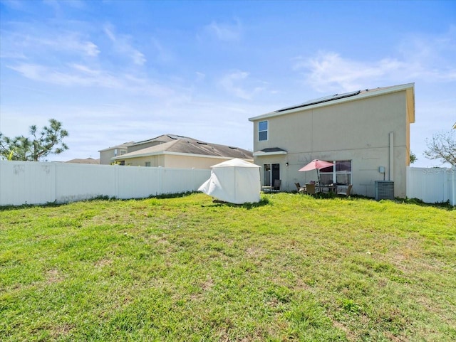 rear view of house with stucco siding, a fenced backyard, a yard, cooling unit, and solar panels