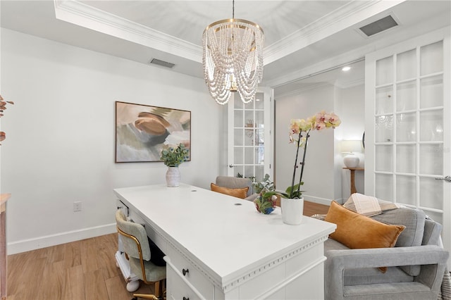 office space with light wood-type flooring, a raised ceiling, an inviting chandelier, and ornamental molding