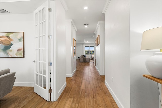 hall featuring light wood-type flooring, visible vents, baseboards, and ornamental molding