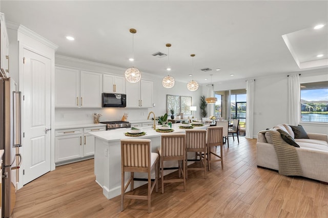 kitchen featuring visible vents, a breakfast bar, stove, black microwave, and open floor plan