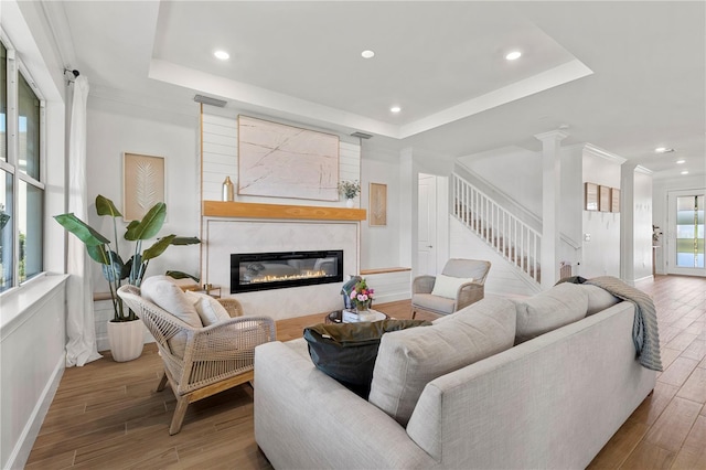 living area featuring stairs, a raised ceiling, wood finished floors, and a fireplace