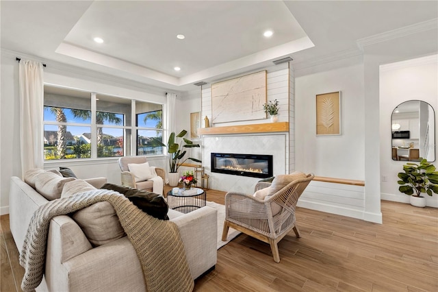 living area with visible vents, baseboards, a tray ceiling, a fireplace, and wood finished floors