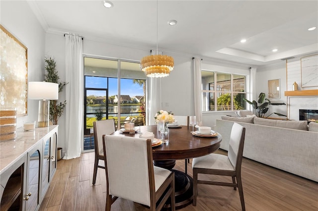 dining area featuring a fireplace, recessed lighting, ornamental molding, light wood-style floors, and a raised ceiling