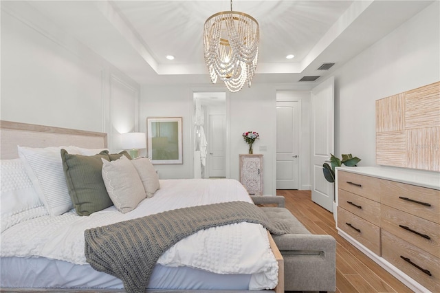 bedroom featuring wood finished floors, visible vents, an inviting chandelier, a tray ceiling, and recessed lighting