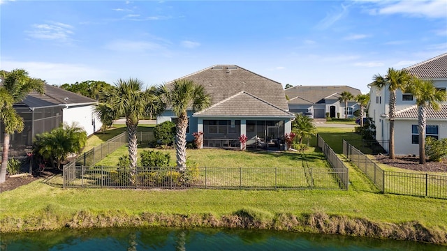 rear view of house featuring a water view, a lawn, a fenced backyard, and a sunroom