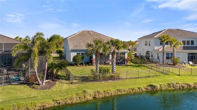 rear view of house with stucco siding, a water view, a lawn, and a fenced backyard