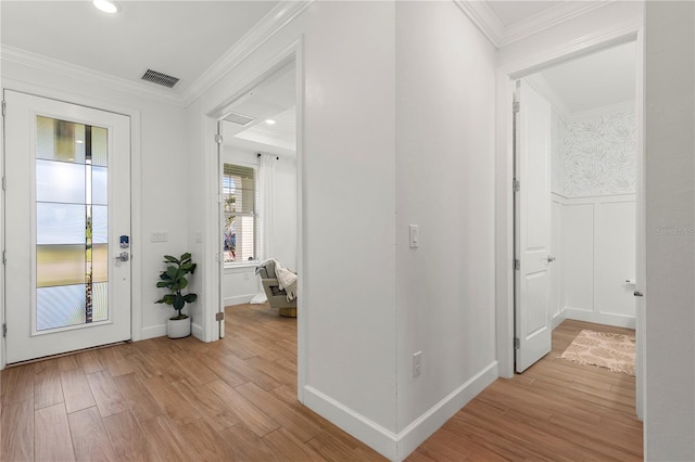 foyer entrance featuring visible vents, light wood-style flooring, crown molding, and a wainscoted wall