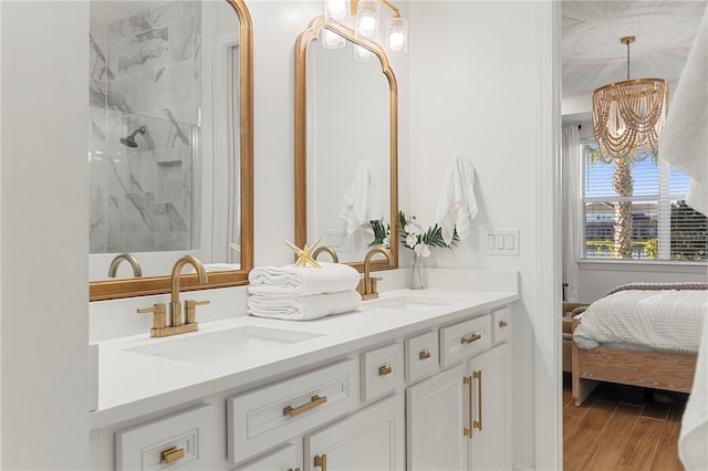 ensuite bathroom featuring tiled shower, double vanity, a notable chandelier, and a sink