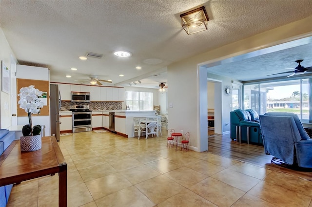 kitchen with tasteful backsplash, open floor plan, light countertops, appliances with stainless steel finishes, and white cabinetry