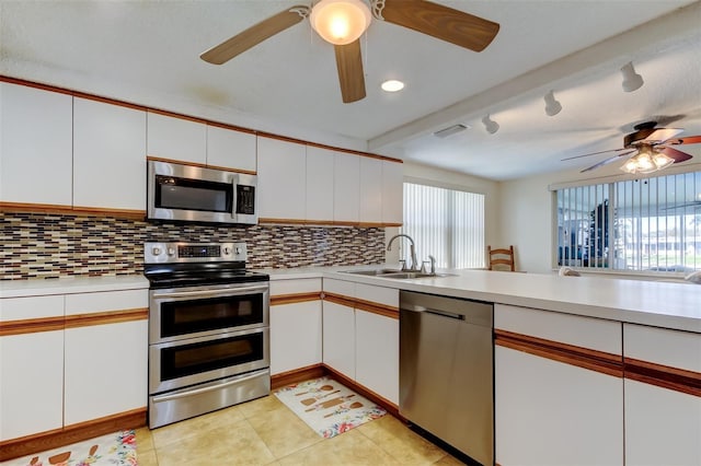 kitchen with light countertops, decorative backsplash, white cabinets, stainless steel appliances, and a sink