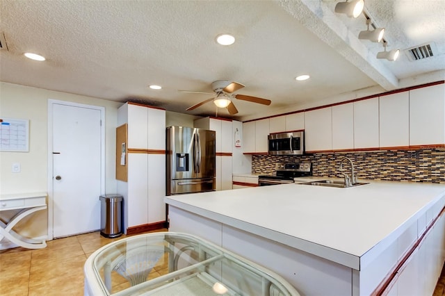 kitchen featuring backsplash, light countertops, appliances with stainless steel finishes, a peninsula, and a sink