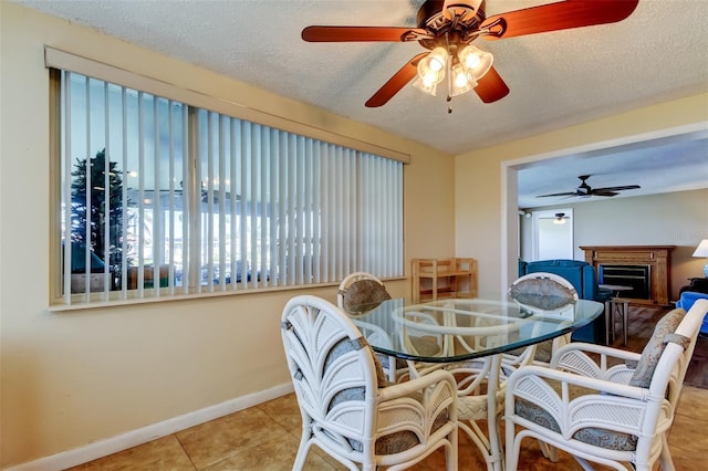 dining space with tile patterned floors, a ceiling fan, a textured ceiling, a fireplace, and baseboards