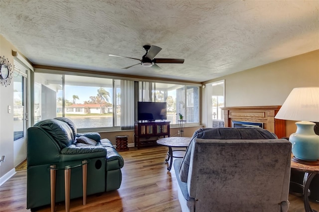 living room featuring a ceiling fan, a textured ceiling, wood finished floors, a fireplace, and baseboards