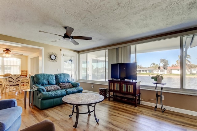 living area featuring a textured ceiling, wood finished floors, baseboards, and ceiling fan