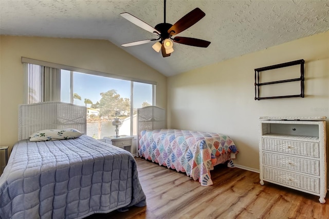 bedroom with a ceiling fan, lofted ceiling, wood finished floors, and a textured ceiling