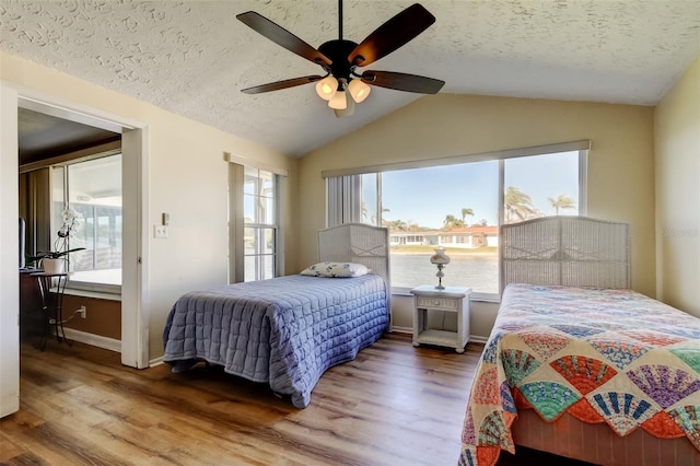 bedroom with lofted ceiling, a textured ceiling, wood finished floors, and a ceiling fan