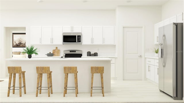 kitchen featuring white cabinets, stainless steel appliances, a kitchen bar, and light countertops