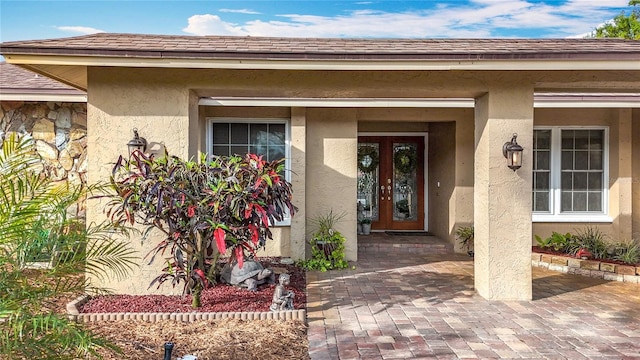 doorway to property featuring a shingled roof, french doors, and stucco siding