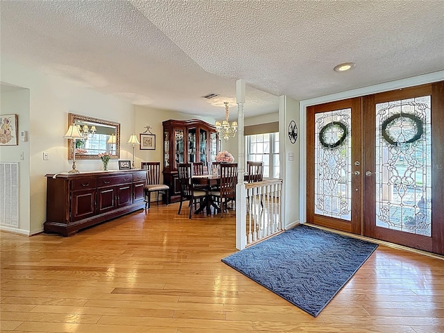 foyer entrance featuring baseboards, light wood-style flooring, french doors, an inviting chandelier, and a textured ceiling