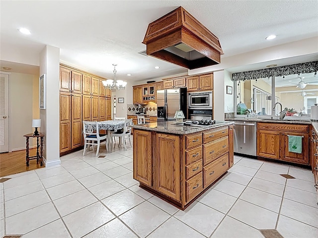 kitchen featuring brown cabinets, dark stone countertops, appliances with stainless steel finishes, an inviting chandelier, and light tile patterned floors