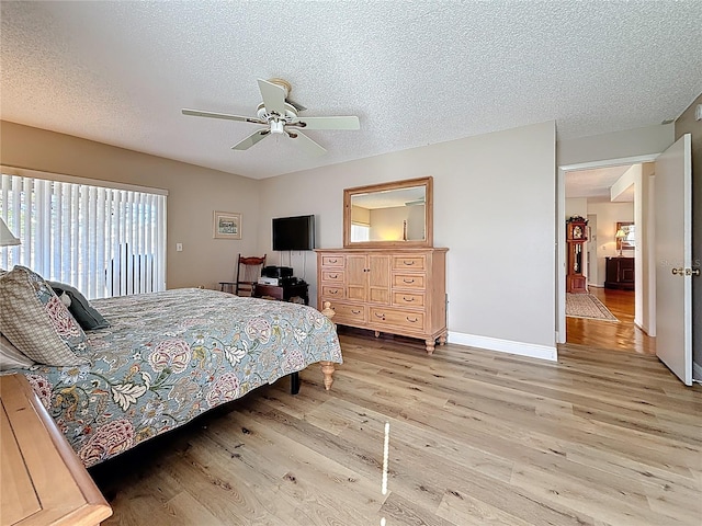 bedroom with light wood finished floors, a textured ceiling, baseboards, and a ceiling fan