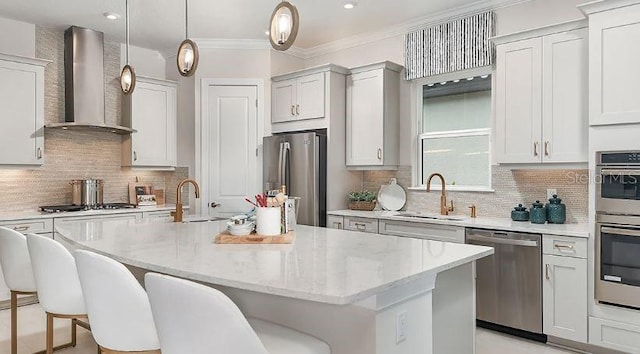 kitchen featuring wall chimney range hood, an island with sink, appliances with stainless steel finishes, and a sink