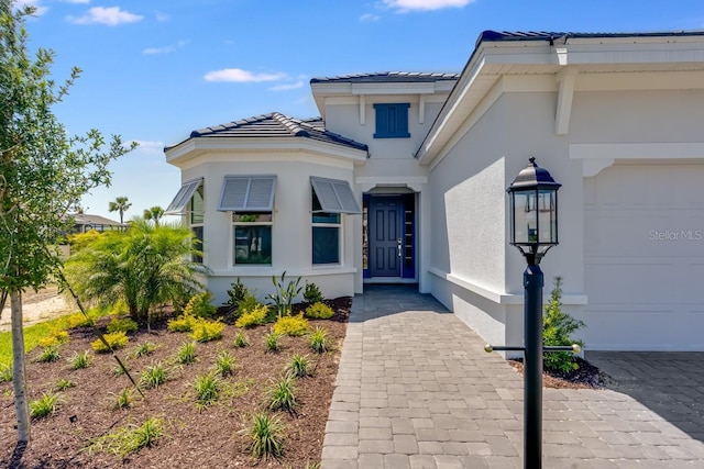 view of exterior entry with stucco siding, a tiled roof, and a garage