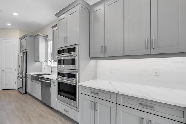 kitchen featuring a sink, gray cabinetry, appliances with stainless steel finishes, light stone countertops, and recessed lighting