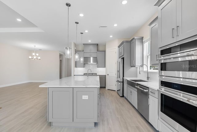 kitchen with under cabinet range hood, a sink, gray cabinetry, tasteful backsplash, and appliances with stainless steel finishes