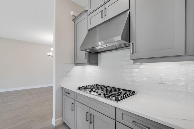 kitchen featuring baseboards, gray cabinetry, under cabinet range hood, and stainless steel gas cooktop