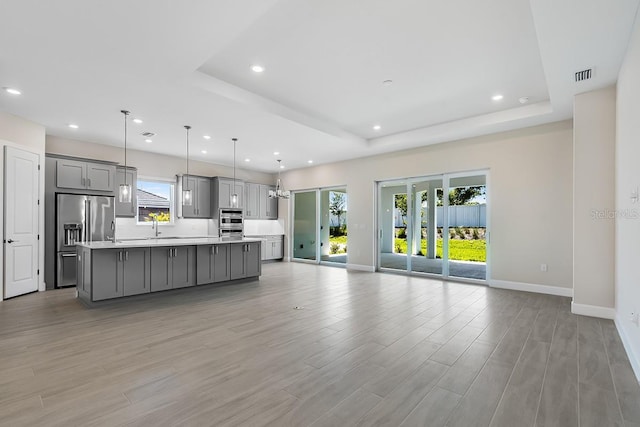 unfurnished living room featuring a tray ceiling, visible vents, baseboards, recessed lighting, and light wood-style floors
