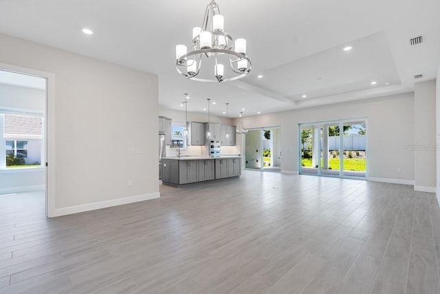 unfurnished living room with baseboards, a notable chandelier, a sink, and light wood finished floors