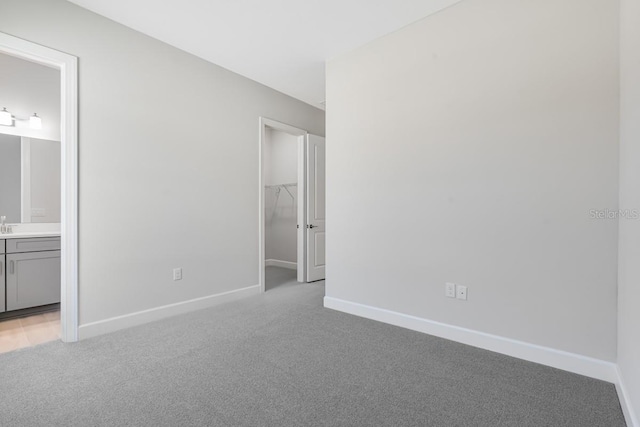 unfurnished bedroom with a spacious closet, light carpet, and baseboards