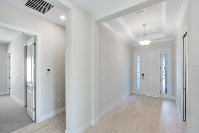 foyer with a tray ceiling, light wood-type flooring, visible vents, and ornamental molding