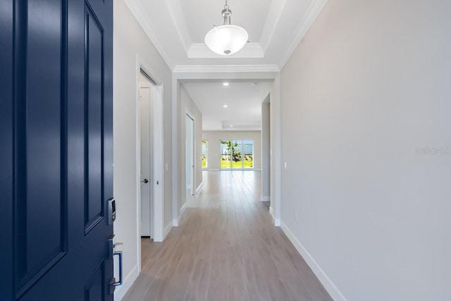 hallway featuring a tray ceiling, baseboards, recessed lighting, light wood-style floors, and ornamental molding