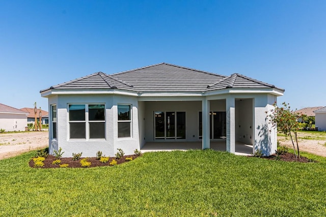 rear view of house with a yard, a tile roof, a patio, and stucco siding
