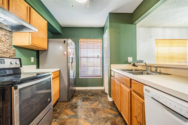 kitchen with under cabinet range hood, light countertops, appliances with stainless steel finishes, a textured ceiling, and a sink