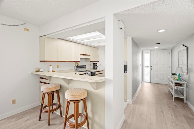 kitchen featuring light wood-type flooring, electric stove, under cabinet range hood, a breakfast bar area, and light countertops