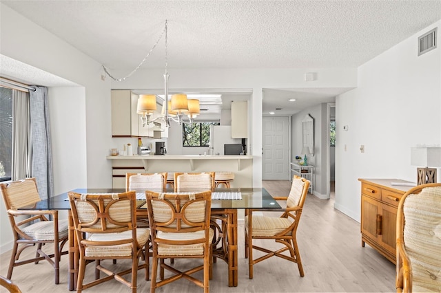 dining room featuring a notable chandelier, visible vents, a textured ceiling, and light wood-style floors