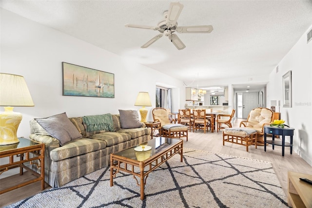 living room with light wood finished floors, ceiling fan with notable chandelier, and a textured ceiling