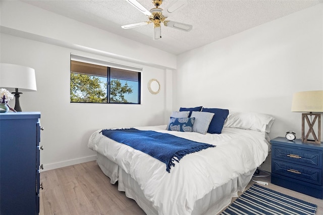 bedroom with baseboards, ceiling fan, a textured ceiling, and light wood-style floors