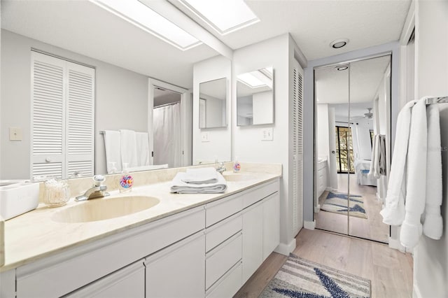 bathroom with wood finished floors, baseboards, double vanity, a skylight, and a sink