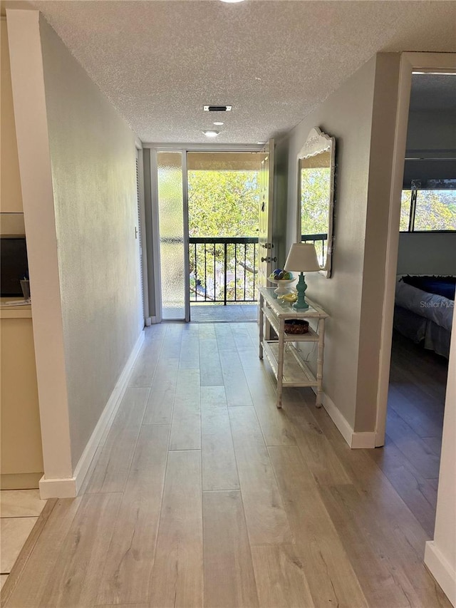 corridor with floor to ceiling windows, wood finished floors, baseboards, and a textured ceiling