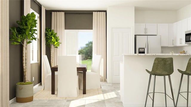 kitchen with fridge with ice dispenser, a kitchen bar, light stone counters, stainless steel microwave, and white cabinetry