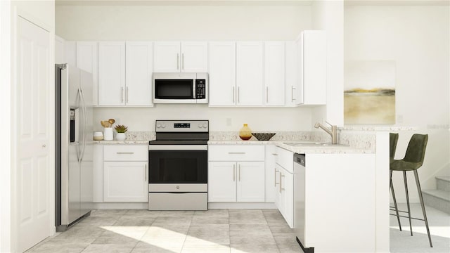 kitchen featuring a breakfast bar area, light stone countertops, a sink, stainless steel appliances, and white cabinetry