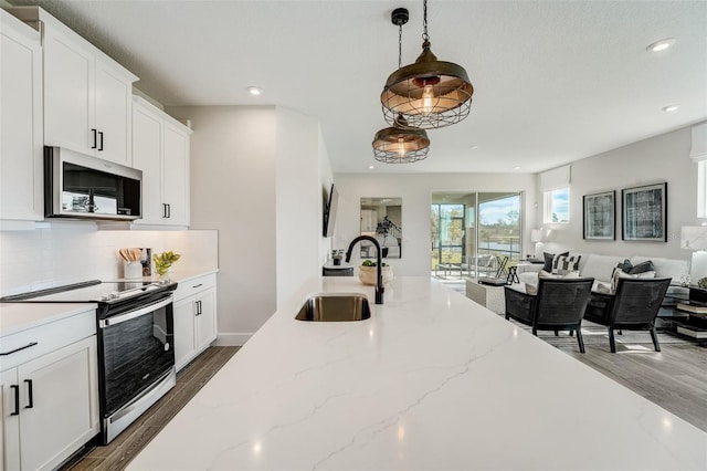 kitchen featuring a sink, stainless steel microwave, backsplash, open floor plan, and electric range oven