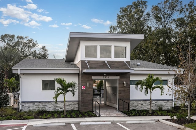 contemporary house with uncovered parking, stone siding, stucco siding, and a gate