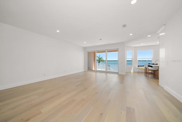 spare room with recessed lighting, light wood-type flooring, a water view, and baseboards