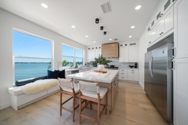 kitchen featuring stainless steel built in fridge, visible vents, a breakfast bar, a sink, and a center island